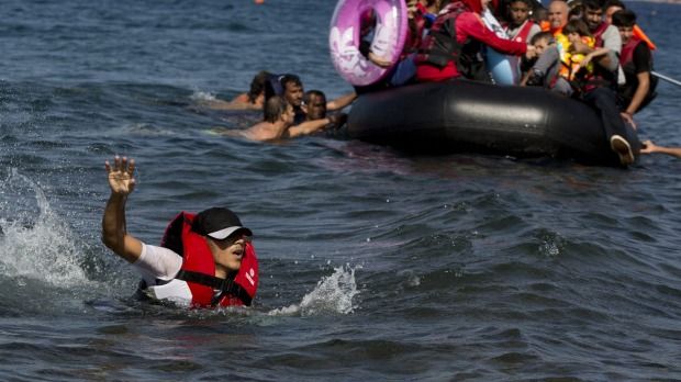 A Syrian man swims in front of a dinghy full of refugees. Photo: Petros Giannakouris 